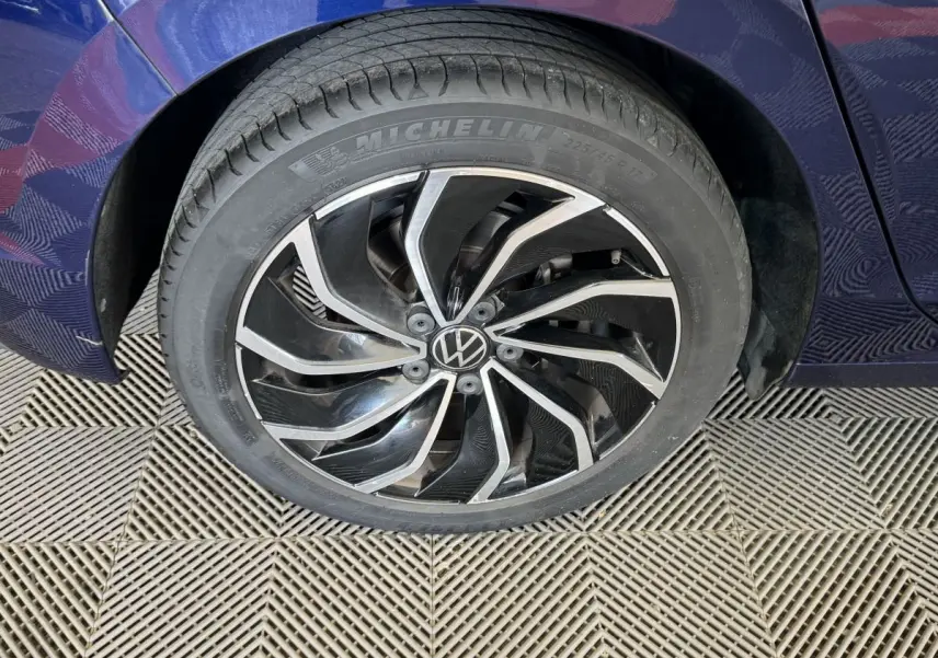 Gros plan sur la roue avant gauche avec jante alliage noire et argentée du Volkswagen Golf bleu 2021.