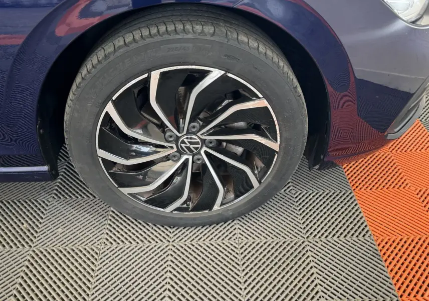 Gros plan sur la roue avant gauche d'une Volkswagen Golf bleu foncé avec jante alliage noire et argentée.