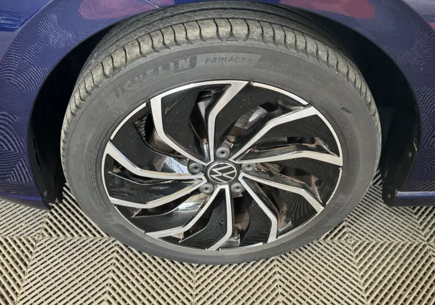 Gros plan sur la roue avant droite bleu métallisé d'une Volkswagen Golf avec jante alliage noire et argentée.