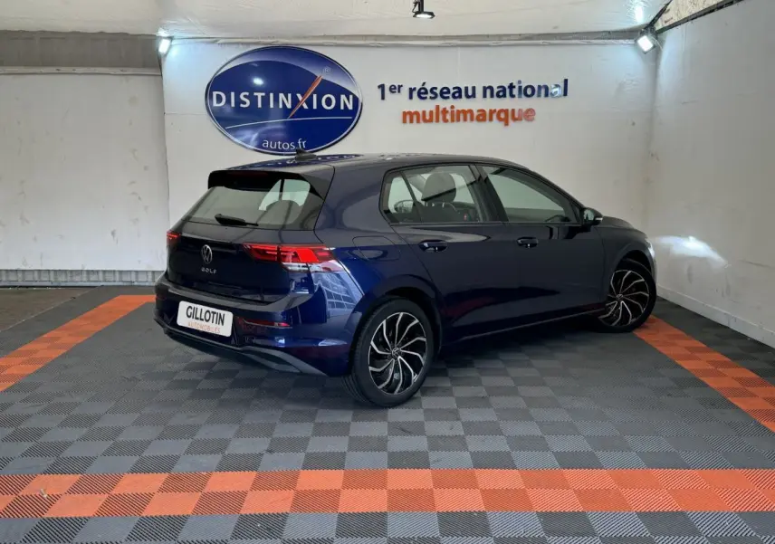 Volkswagen Golf bleu vue 3/4 arrière droit dans un showroom avec jantes noires et rouges.