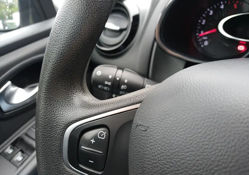 Gros plan sur le volant et la commande de régulateur de vitesse d'une Renault Clio IV Société blanche, tableau de bord partiellement visible.