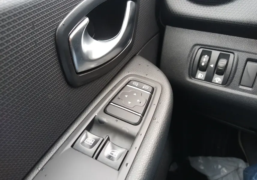 Gros plan sur la commande des vitres électriques et la poignée intérieure côté gauche d'une Renault Clio IV Société blanche.