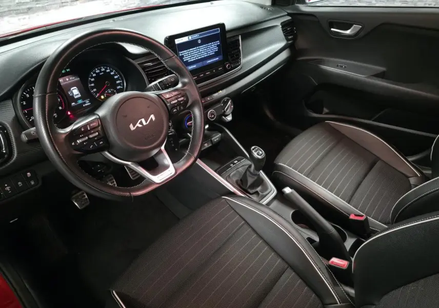 Vue intérieure côté conducteur de la KIA Rio rouge 2022, volant cuir GT Line et console centrale avec écran tactile.