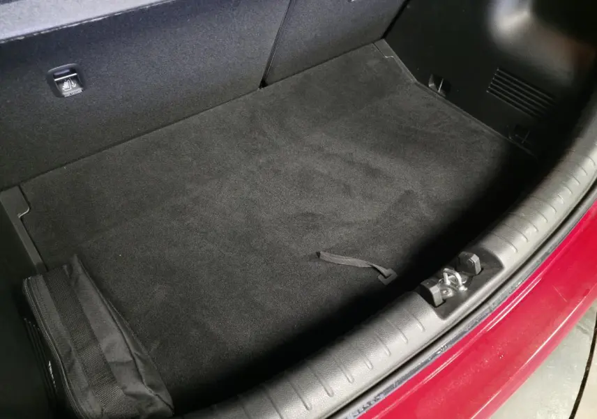 Coffre ouvert vu de dessus d'une KIA RIO rouge 2022, avec tapis noir et bordure de coffre en plastique.