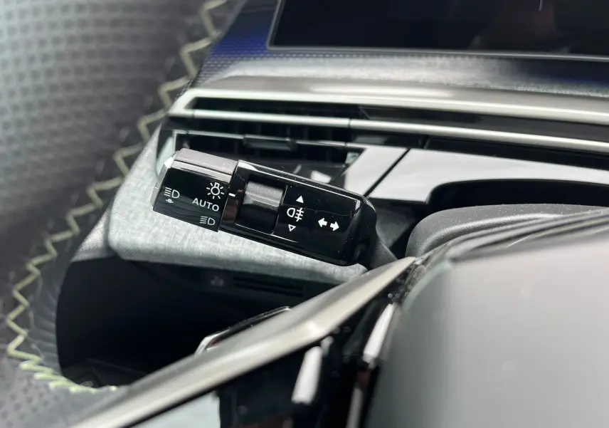Gros plan sur la commande des feux et clignotants à gauche du volant dans l'habitacle noir du Peugeot 3008 Hybrid 2025.