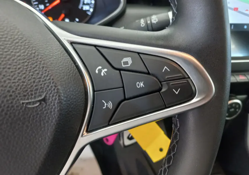 Gros plan sur les commandes au volant côté droit d'une Renault Clio Business blanche, avec écran tactile visible en arrière-plan.