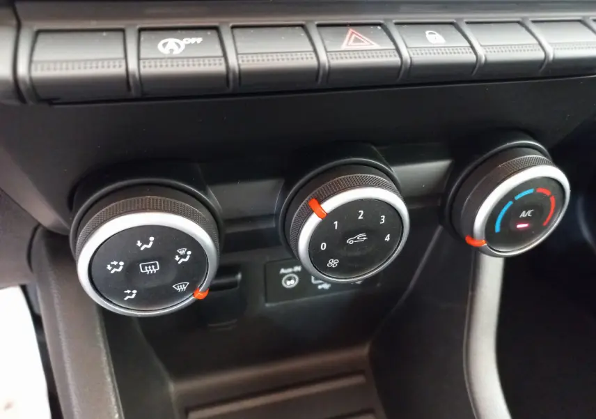 Gros plan sur les commandes de climatisation de la Renault Clio Business blanche, avec réglages rotatifs noirs et indicateurs rouges.