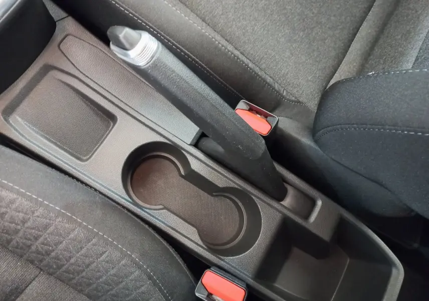 Vue rapprochée de la console centrale noire avec frein à main et porte-gobelets entre les sièges tissu gris de la Renault Clio Business.