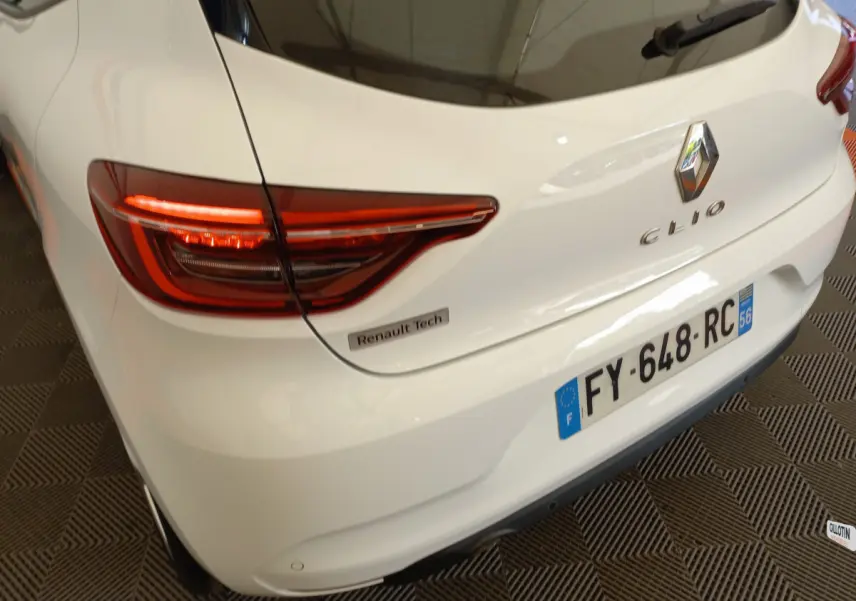 Vue 3/4 arrière droite d'une Renault Clio blanche avec feux LED et badge Renault Tech visible sur le coffre.