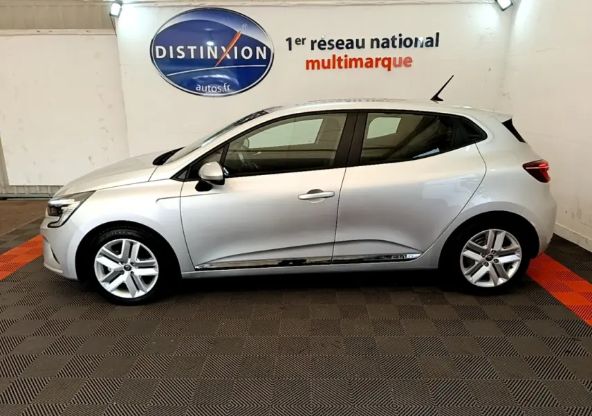 Profil côté gauche d'une Renault Clio Business E-Tech hybride 140 gris clair, dans un showroom avec logo Distinxion en arrière-plan.
