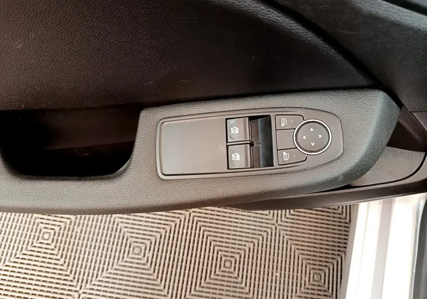 Gros plan sur la commande des vitres et rétroviseurs côté conducteur d'une Renault Clio Business E-Tech gris clair.