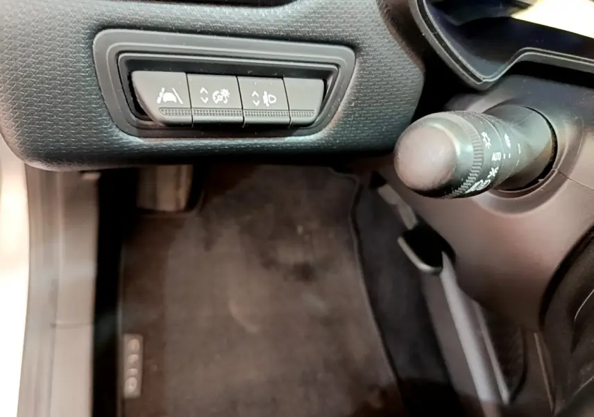 Vue rapprochée des commandes d'assistance et du commodo d'éclairage côté gauche dans l'habitacle de la Renault Clio gris clair.
