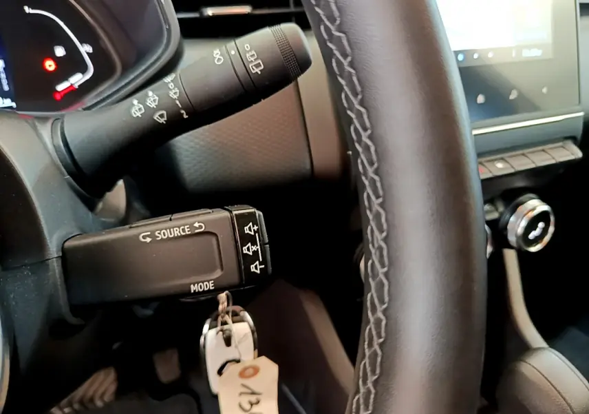 Gros plan sur le volant cuir noir et la commande multimédia à gauche dans l'habitacle d'une Renault Clio gris clair hybride.