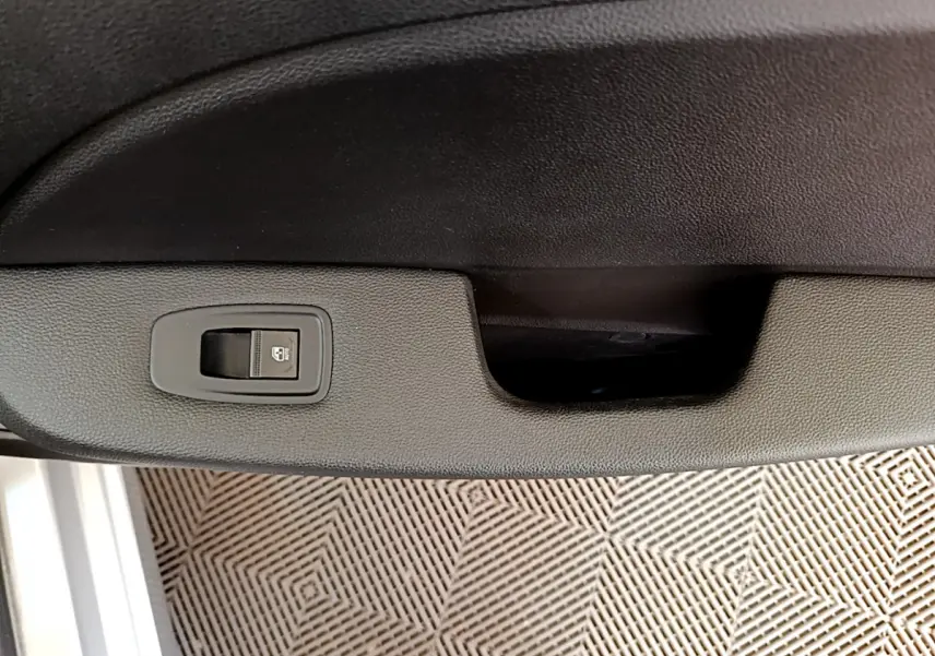 Gros plan sur la commande de verrouillage des portes intégrée à la garniture intérieure d'une Renault Clio gris clair.