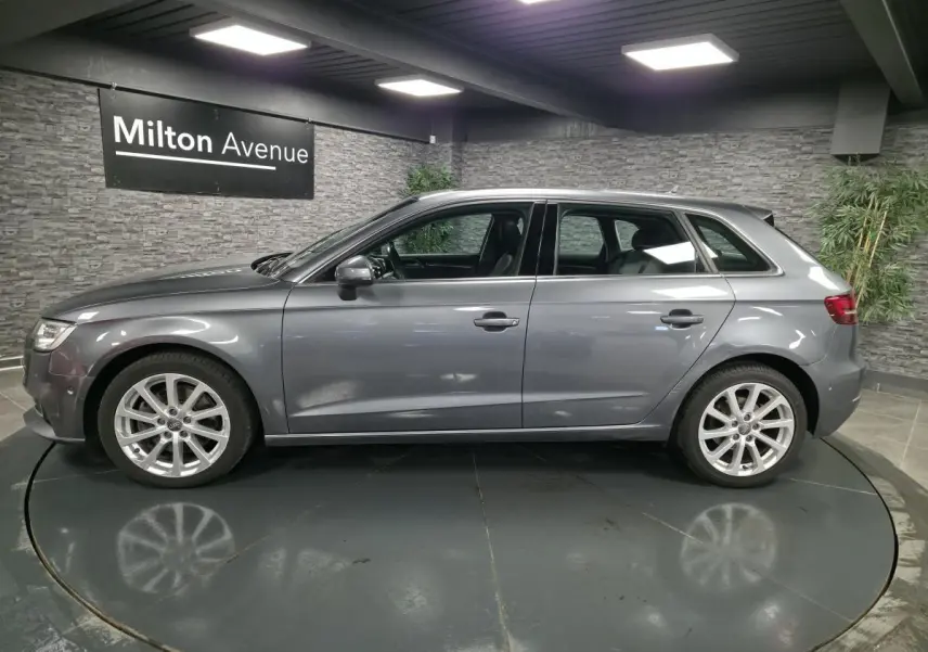 Audi A3 Sportback gris vue de profil côté gauche dans un showroom avec jantes aluminium 17 pouces.