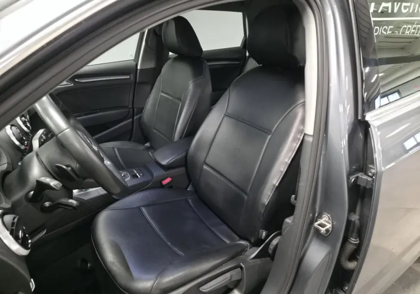 Vue intérieure côté conducteur de l'Audi A3 Sportback gris, sièges en similicuir noir et tableau de bord visible.