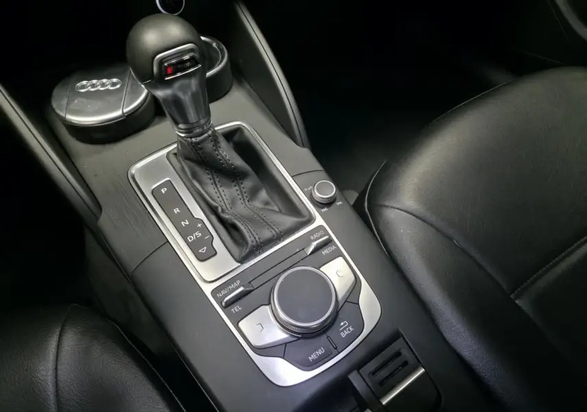 Gros plan sur la console centrale noire de l'Audi A3 Sportback, mettant en valeur le levier de vitesses automatique et les commandes multimédia.