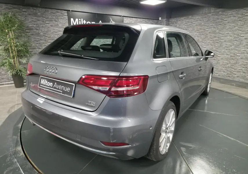 Audi A3 Sportback gris vue 3/4 arrière droit dans un showroom avec jantes aluminium 17 pouces.