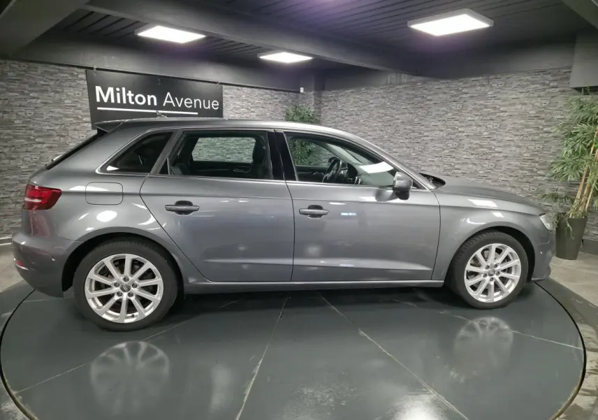 Profil côté gauche d'une Audi A3 Sportback gris métallisé 2017 dans un showroom avec jantes aluminium 17 pouces.