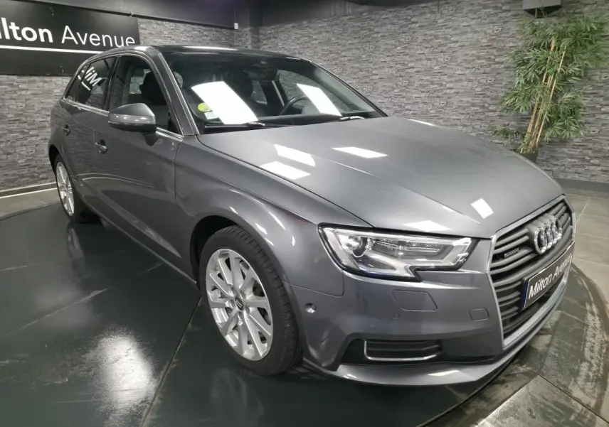 Audi A3 Sportback gris métallisé vue 3/4 avant droit dans un showroom avec éclairage intérieur.