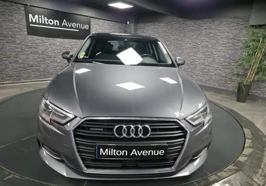 Audi A3 Sportback gris vue de face en intérieur avec calandre hexagonale et logo quatre anneaux lumineux.