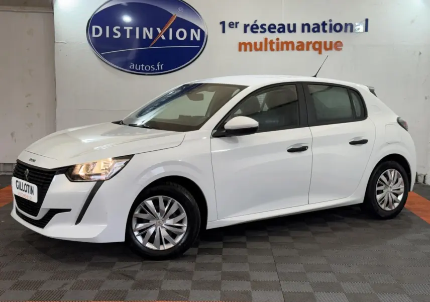 Peugeot 208 blanc vue de profil droit en intérieur, avec phares allumés et jantes alliage simples.