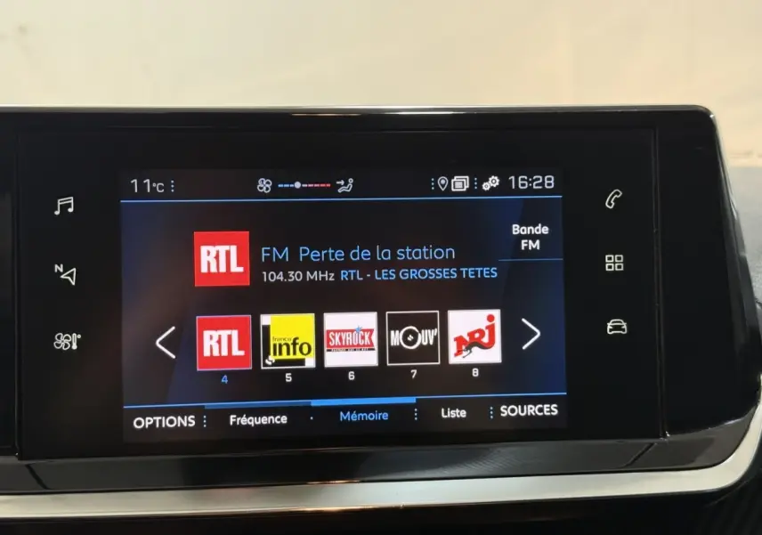 Écran tactile central de la Peugeot 208 blanc, affichant les stations radio FM avec interface moderne.