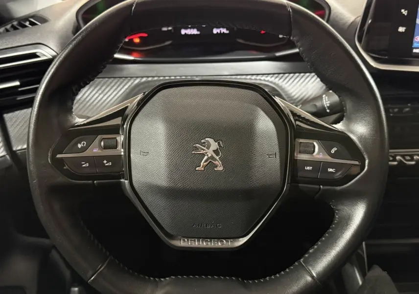 Volant noir de Peugeot 208 1.5 BlueHDi 2021 vu de face avec commandes intégrées et tableau de bord en arrière-plan.