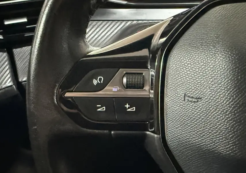 Gros plan sur les commandes gauche du volant cuir noir de la Peugeot 208 1.5 BlueHDi 100 S&S Premium 2021.