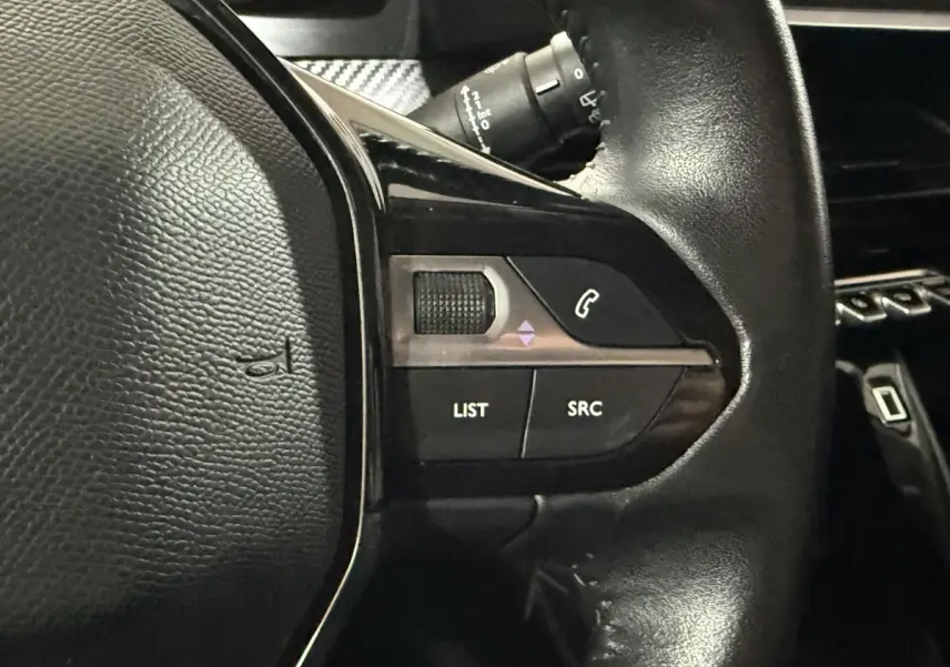 Gros plan sur les commandes gauche du volant noir de la Peugeot 208 1.5 BlueHDi 100 S&S Premium, avec boutons LIST et SRC.