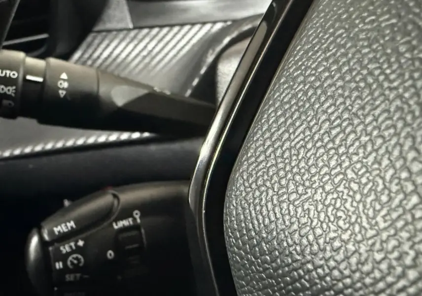 Gros plan sur le volant noir texturé et la commande de régulateur de vitesse d'une Peugeot 208 blanche, intérieur côté conducteur.