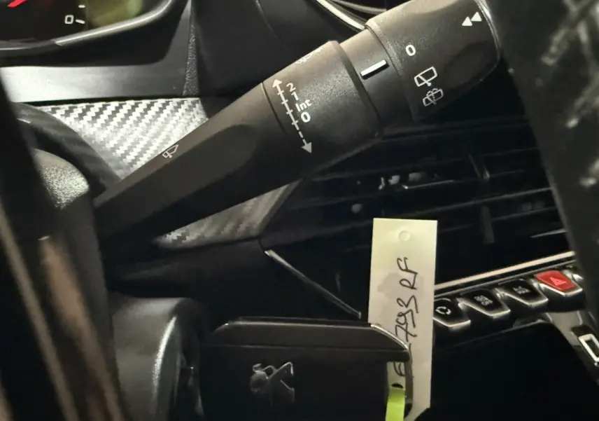 Gros plan sur la commande d’essuie-glace et la console centrale noire du tableau de bord d’une Peugeot 208 blanche.