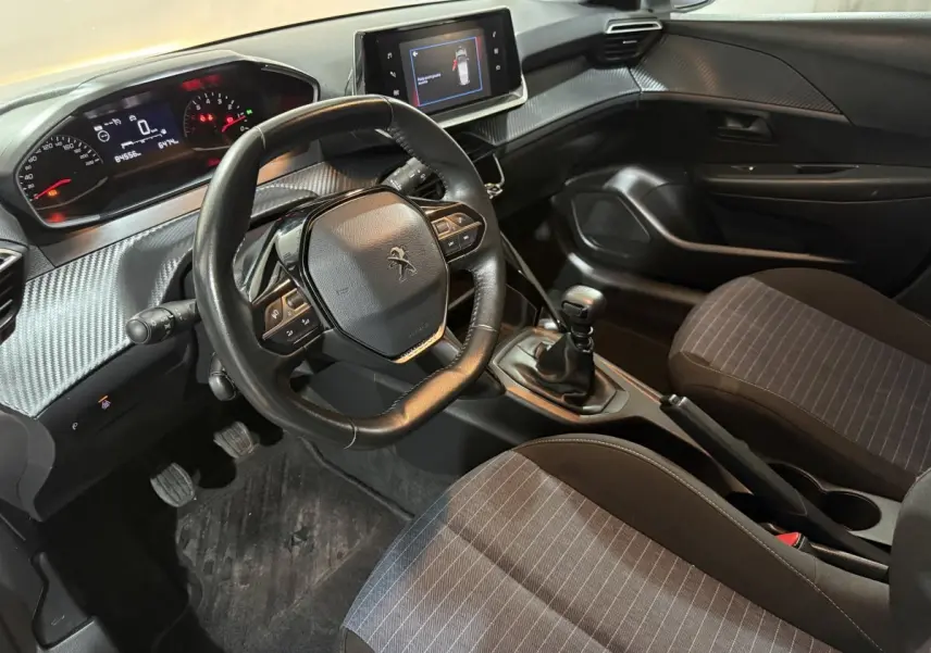 Vue intérieure côté conducteur de la Peugeot 208 blanche, montrant le volant compact, tableau de bord numérique et levier de vitesse manuel.