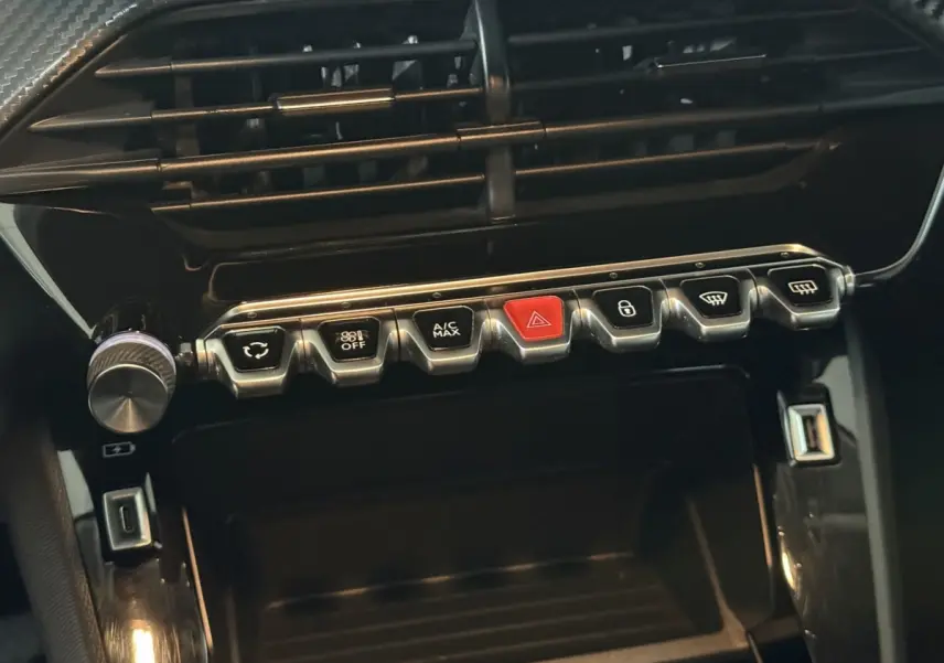 Gros plan sur la console centrale noire de la Peugeot 208 avec rangée de boutons chromés et USB visible.