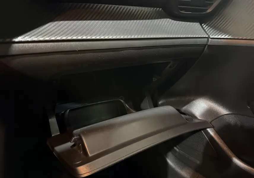 Gros plan de la boîte à gants ouverte côté passager dans l’habitacle noir de la Peugeot 208 blanche.