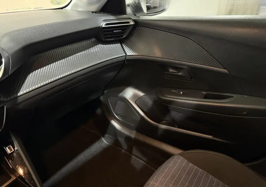 Intérieur côté passager de la Peugeot 208 1.5 BlueHDi 2021, tableau de bord noir avec finition carbone et porte noir.