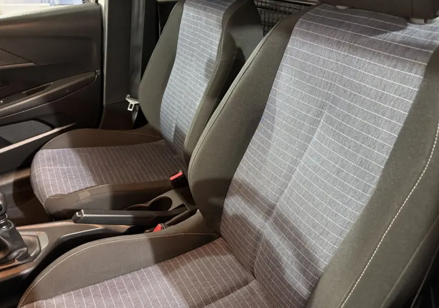 Vue intérieure rapprochée des sièges avant gris à motifs rayés de la Peugeot 208 1.5 BlueHDi 2021 avec cloison métallique arrière.