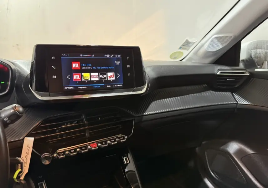 Vue intérieure côté passager du tableau de bord noir de la Peugeot 208 avec écran tactile central affichant une radio FM.