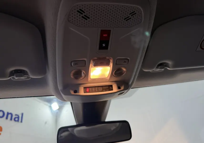 Vue intérieure en contre-plongée du plafonnier gris clair avec éclairage et bouton SOS allumé dans une Peugeot 208 blanche.