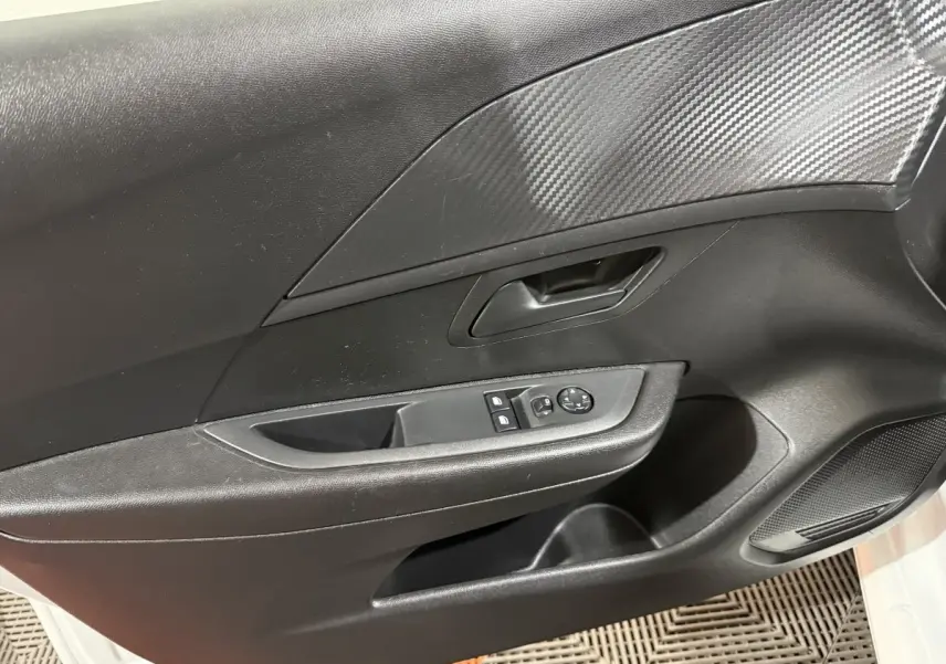 Vue rapprochée de la porte avant gauche intérieure noire avec insert imitation carbone et commandes électriques.