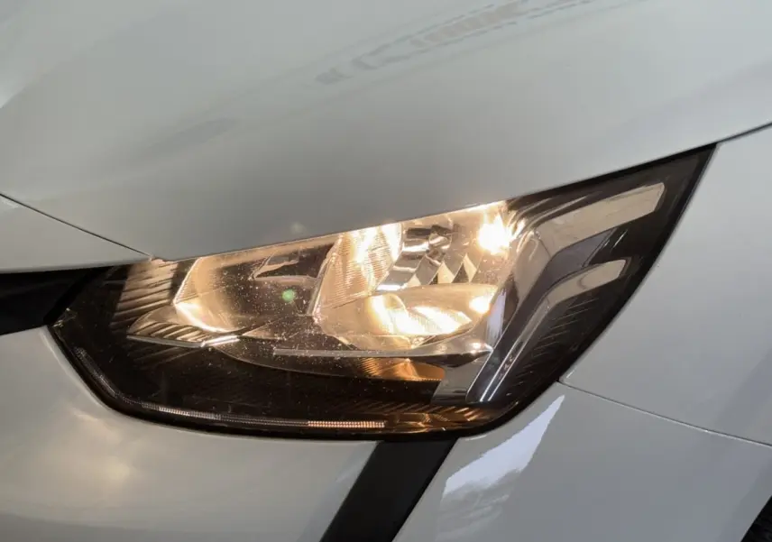 Gros plan sur le phare avant droit allumé d'une Peugeot 208 blanche, soulignant les détails du bloc optique.