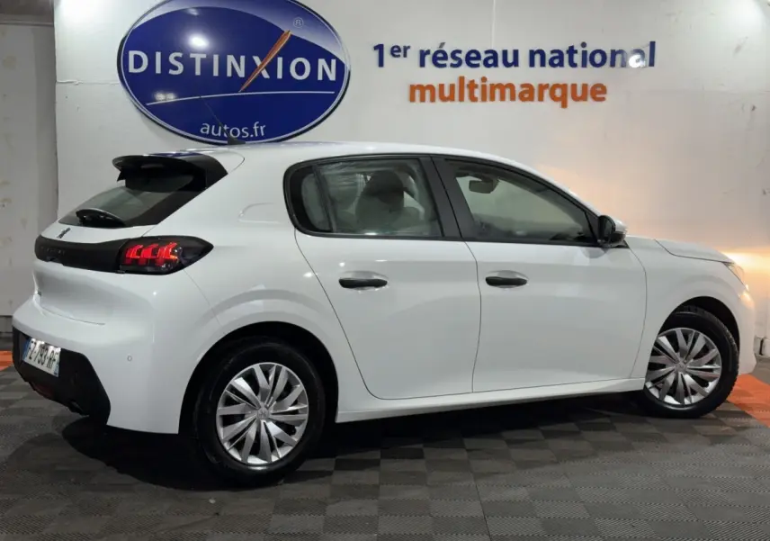 Peugeot 208 blanche vue de profil droit en intérieur, avec feux arrière LED et jantes alliage visibles.