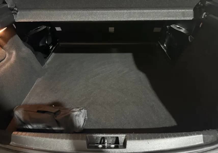 Vue intérieure du coffre spacieux et propre d'une Peugeot 208 blanche, avec un tapis noir et une trousse rangée.