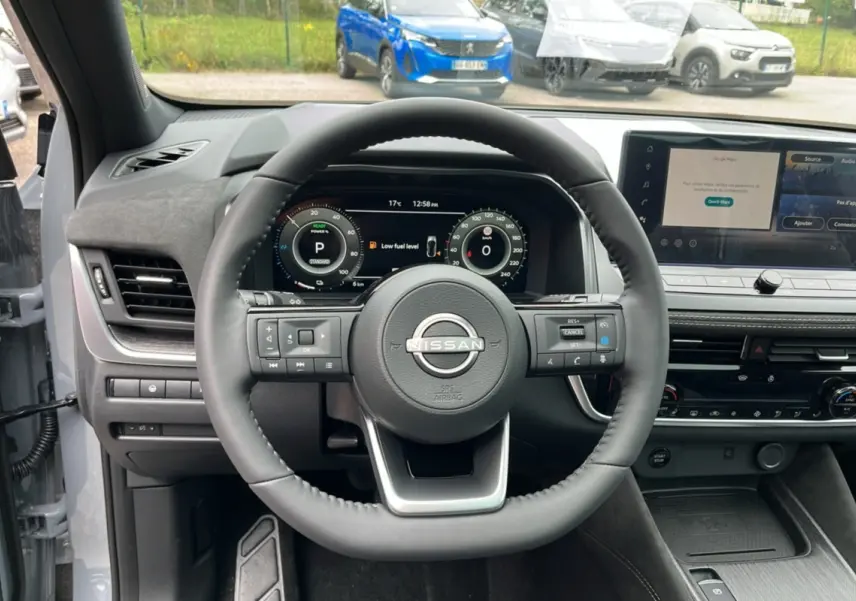 Vue intérieure centrée sur le volant cuir du Nissan Qashqai E-POWER 205 Tekna Plus avec tableau de bord numérique et écran tactile.