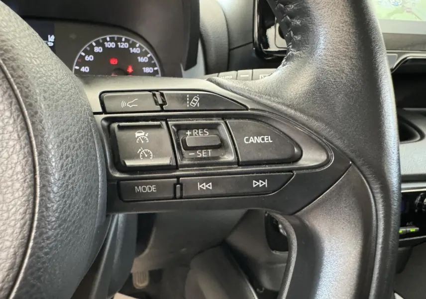 Gros plan sur les commandes au volant cuir noir de la Toyota Yaris hybride 2022, avec tableau de bord et écran tactile visibles.