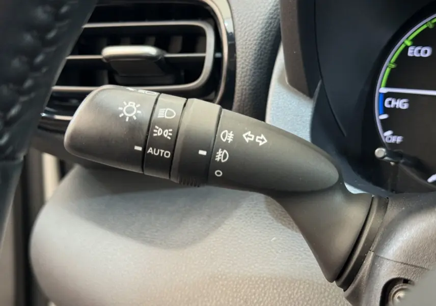 Gros plan sur la commande des phares et clignotants à gauche du volant dans l’habitacle noir de la Toyota Yaris hybride blanche 2022.