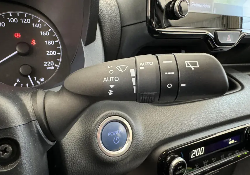 Gros plan sur la commande d’essuie-glace et bouton Power bleu du tableau de bord noir de la Toyota Yaris hybride 2022.