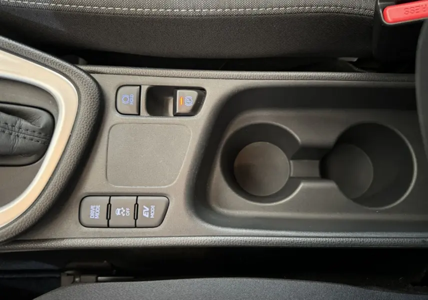 Vue rapprochée de la console centrale noire de la Toyota Yaris hybride avec boutons de modes de conduite et frein à main électrique.