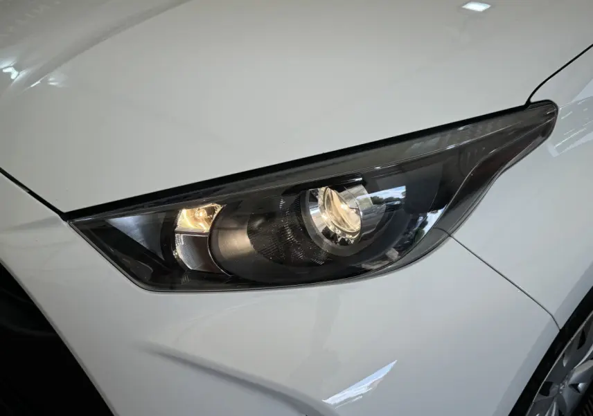 Gros plan sur le phare avant droit allumé d'une Toyota Yaris hybride blanche de 2022, finition Dynamic Business.