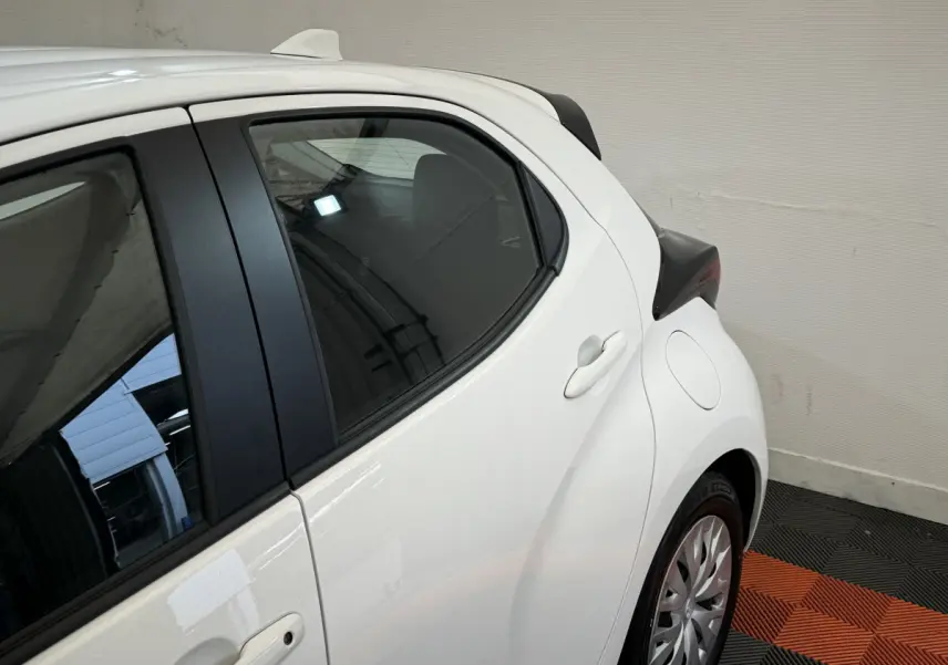 Vue côté droit arrière de la Toyota Yaris hybride blanche 2022, mettant en valeur la porte arrière et le passage de roue.